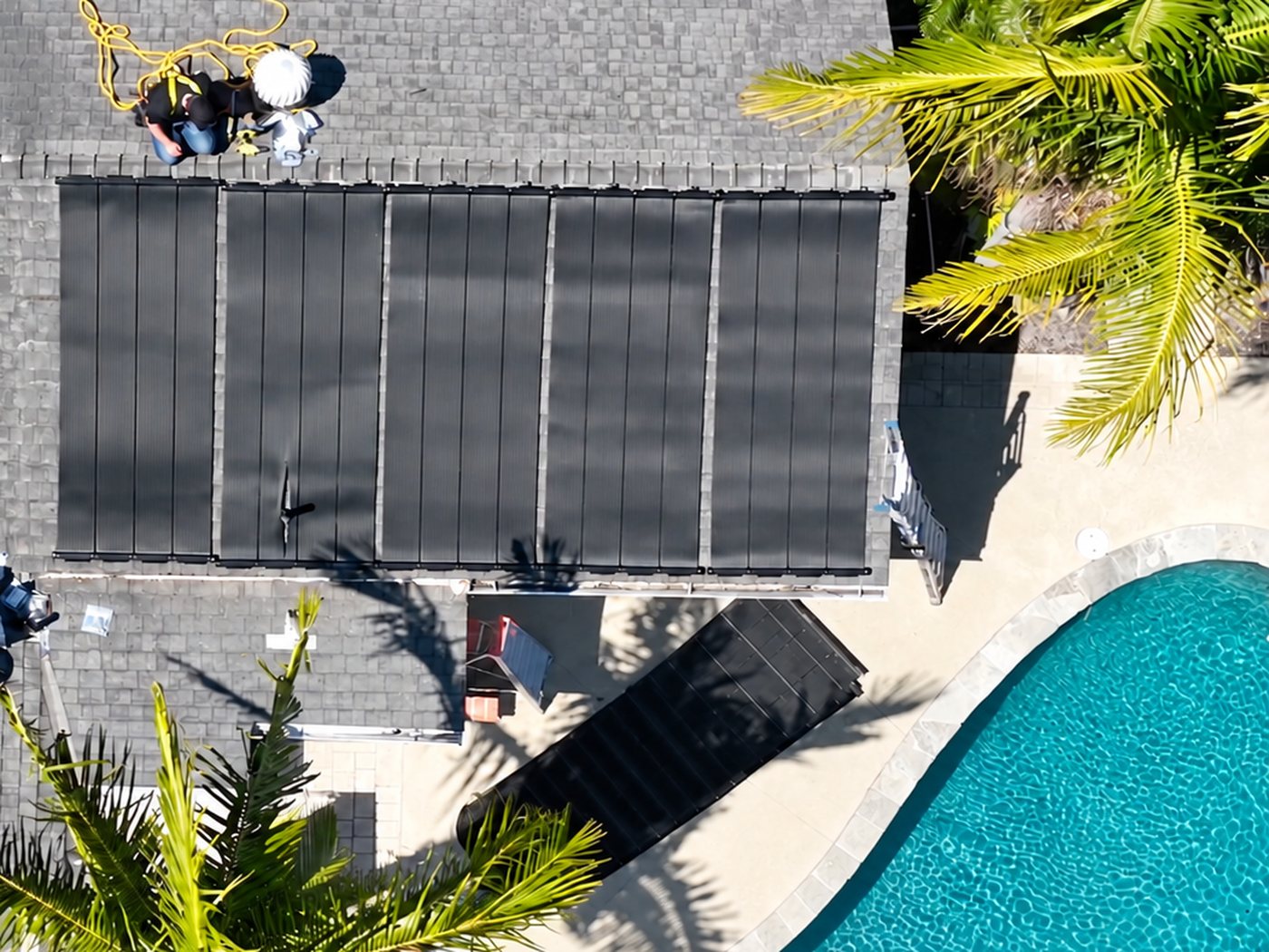 Installers fitting solar heating panels on a roof above a pool