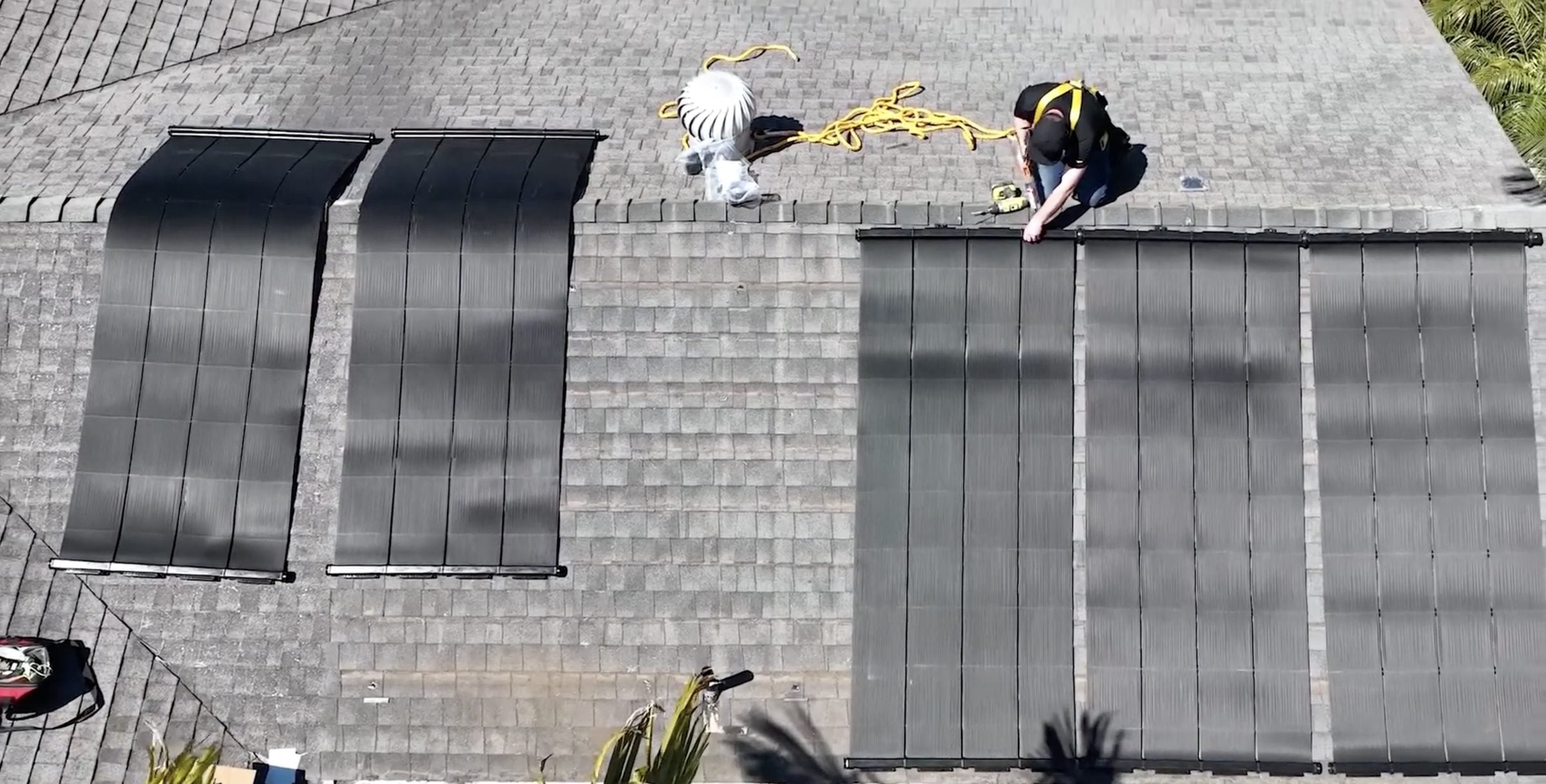 An installer on a shingle roof adding panels beside a row already in place